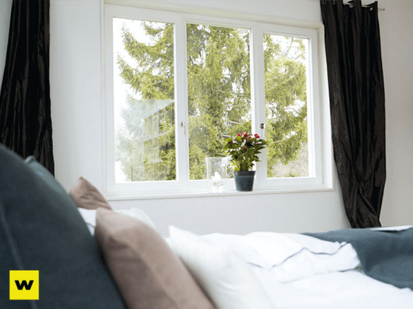 Helles Schlafzimmer mit großen Fenstern, Vorhängen und Topfpflanze auf der Fensterbank.
