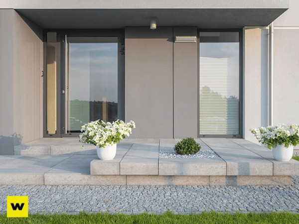 Moderner Hauseingang mit großen Glasfronten, Pflanzkübeln und gefliestem Podest.