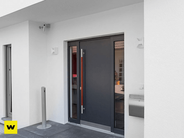 Moderne Haustür aus dunklem Aluminium mit Seitenteil an weißer Hausfassade und Briefkasten.
